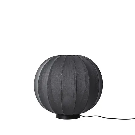 Rund sort lampe med strikket tekstur og moderne æstetik, placeret i gulvhøjde.