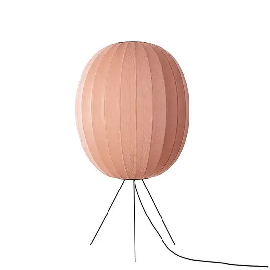 Oval gulvlampe i koralfarve med strikket overflade på trebenet stativ.