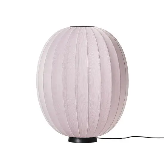 Oval lampe med strikket overflade i lys pink, placeret på en sort base.