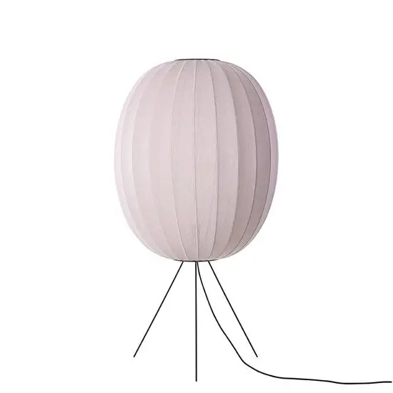 Oval lampe i lys pink med strikket overflade, stående på tre ben.
