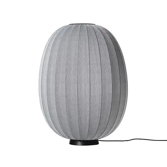 Oval lampe med grå strikket overflade, sort base og ledning til højre.