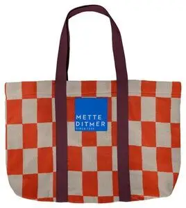 Ternet strandtaske i mørk orange og beige, blå etiket med "METTE DITMER SINCE 1995".
