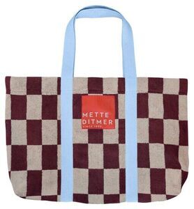 Strandtaske med skakternet mønster i vinrød/beige, blå håndtag og "METTE DITMER" etiket.