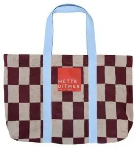 Strandtaske med skakternet mønster i vinrød/beige, blå håndtag og "METTE DITMER" etiket.