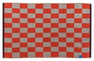 Bademåtte med skakternet mønster i mørk orange og neutral farve, mørk kant og lille blå mærkat.