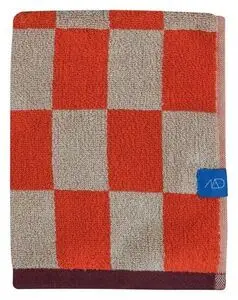 Håndklæde med ternet mønster i mørk orange og beige, blå mærkat med logo.