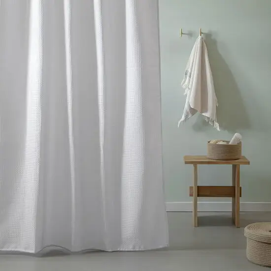 Hvid vaffelmønstret badeforhæng, lang længde. Minimalistisk badeværelse med bænk og lys væg.