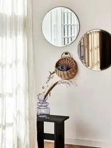 To runde spejle, et bronze og et klart, på væggen. Kurv og vase med tørrede planter på sort bord.