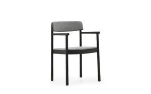 Sort ramme, gråt polstret sæde og ryglæn, armlæn synlige. Normann Copenhagen Timb Armchair.