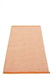 Rektangulært tæppe med orange og hvidt mønster, orange kanter og lille mærke i hjørnet.