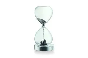 Timeglasformet objekt med klar krop, mørkt granulat indeni, på en cirkulær metalbase.