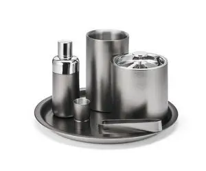 Sølvfarvet barware-sæt med shaker, isspand, tang og kop på rund bakke. Elegant, metallisk finish.
