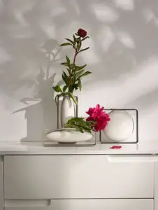 Philippi Float vase i metalramme med blomster, på hvid overflade mod lys væg. Minimalistisk design.