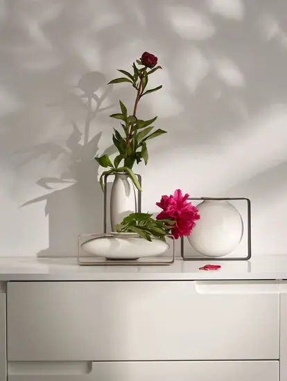 Philippi Float vase i metalramme med blomster, på hvid overflade mod lys væg. Minimalistisk design.