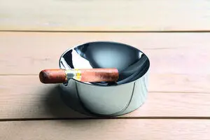 Rund, blank cigar askebæger med cigar på kanten, reflekterende overflade.
