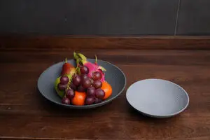 To Philippi Lim skåle på træbord, én med frugt og én tom, med runde design og koncentriske cirkler.