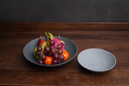 To Philippi Lim skåle på træbord, én med frugt og én tom, med runde design og koncentriske cirkler.