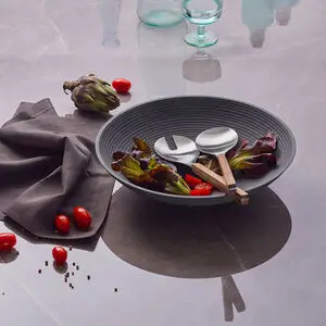 Stor skål med salat, kirsebærtomater og træsalatbestik på marmorbord med serviet og ekstra tomater.