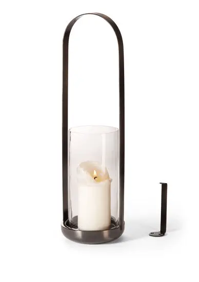 Lanterne med buet håndtag og glas, indeholder et tændt stearinlys. Vægbeslag ved siden af.