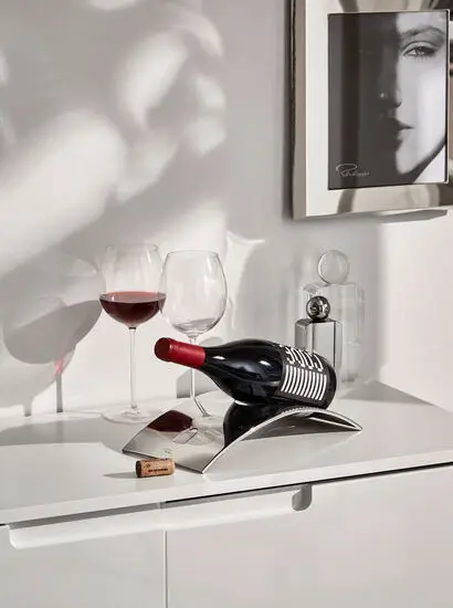 Vinkaraffelholder med buet design, vinflaske vandret, to vinglas, enkelt og stilrent interiør.