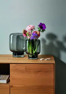 To glasvaser på træbord, én med blomster, én tom. Cylindrisk form, forskellig størrelse.