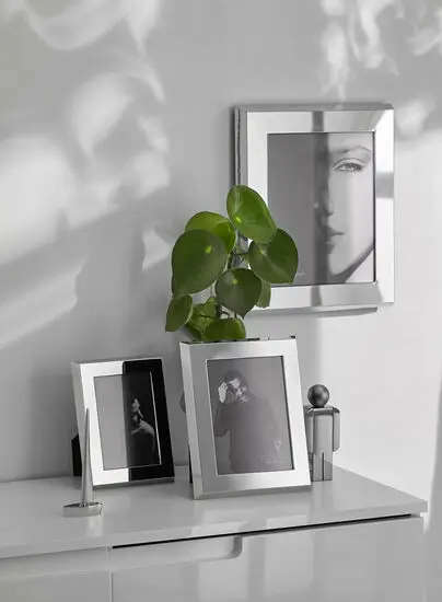 Elegant, spejlblank fotoramme i vertikal orientering med plante og dekorationer på hvid overflade.
