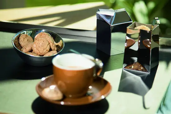 Moderne mælk- og sukkersæt med skinnende overflader, kaffekop og skål med småkager på bordet.