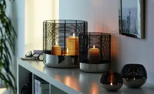 Tealight-holdere med trådramme og metalbund på hylde, skaber varm stemning med tændte lys.