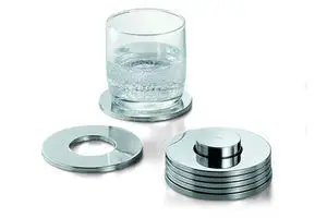 Sæt af 7 metalcoasters med hul i midten. Moderne design, stabelbare. Et glas vand står på en coaster.