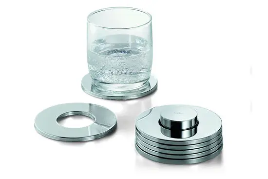 Sæt af 7 metalcoasters med hul i midten. Moderne design, stabelbare. Et glas vand står på en coaster.