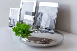 Spejlblank Philippi Elia vase med grøn plante og fotolrammer på glat overflade.
