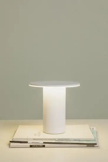 Bordlampe med cylindrisk base, rund top, lyser nedad. Står på flade med magasiner eller bøger.
