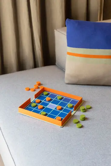 Spil med blå gittermønster, orange kant og brikker i orange og grøn på brættet og omkring det.