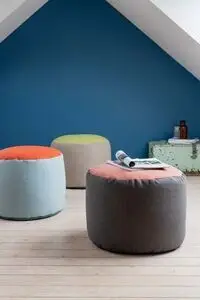 Tre runde puffer på trægulv foran blå væg. To-farvet design; en har et magasin ovenpå.