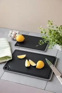 To sorte skærebrætter med grå kanter, citronbåde, kniv, urter og en skål i baggrunden.