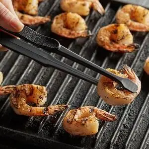 Sorte gourmet pincetter løfter grillede rejer fra en grillpande.