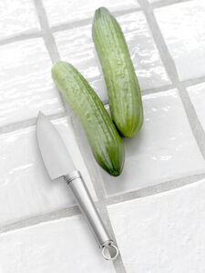 Stålkniv ved siden af to agurker på en flisebelagt overflade. Bladet måler cirka 24,5 cm.