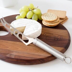 Ostehøvl med buet klinge ligger på skærebræt med ost, grønne druer og kiks.