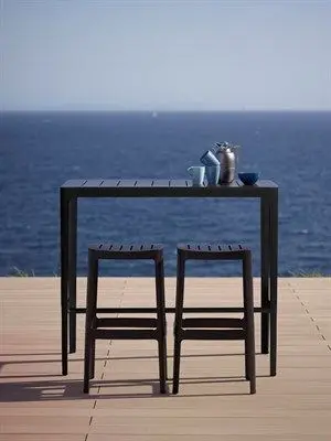 Rektangulært barbord med to stole på træterrasse ved havet. Minimalistisk design til udendørs brug.