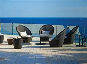 Rundt sofabord på terrasse med udsigt over vandet, omgivet af udendørs loungestole.