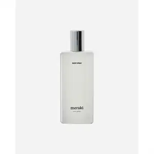 Rektangulær, gennemsigtig flaske med sølvhætte, teksten "ROOM SPRAY" og "meraki" på forsiden.